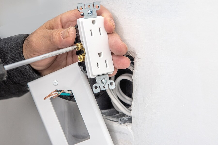 An electrician connects electrical wires to an outlet before installing it.