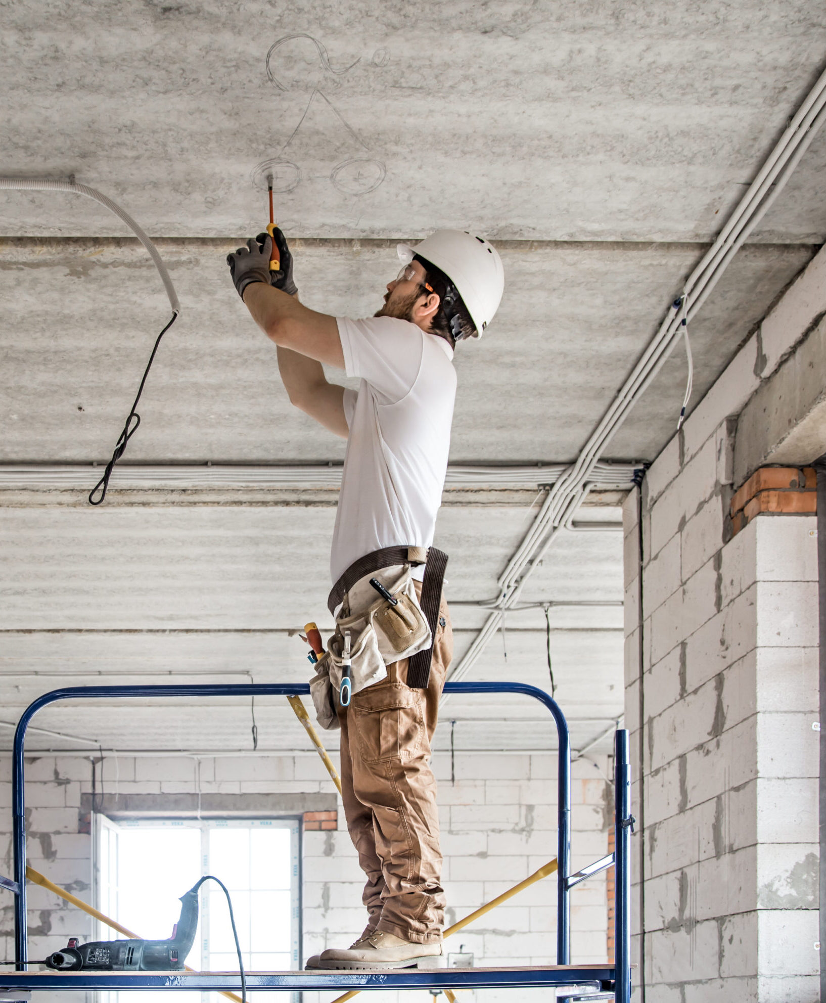 Electrician installer with a tool in his hands, working with cable on the construction site.
